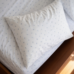 White with subtle blue floral pattern sheets on a bed with wooden headboard
